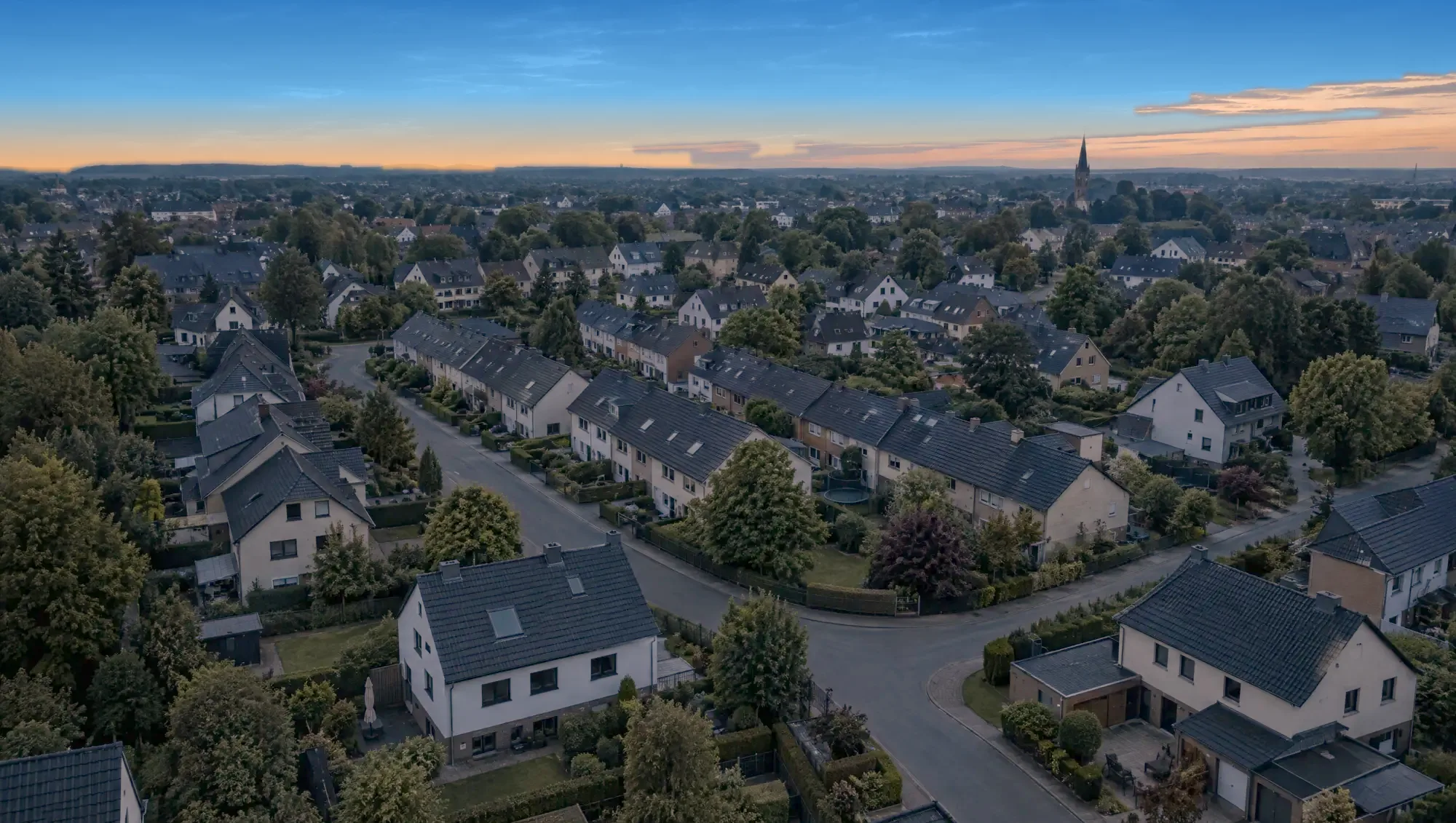 Luftbild eines Wohnviertels bei Dämmerung, nach und nach gehen in vielen Häusern die Lichter an